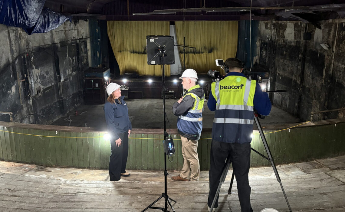 3 people filming a video in front of a cinema screen in a dilapidated auditorium