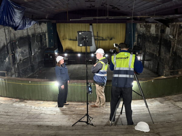 3 people filming a video in front of a cinema screen in a dilapidated auditorium