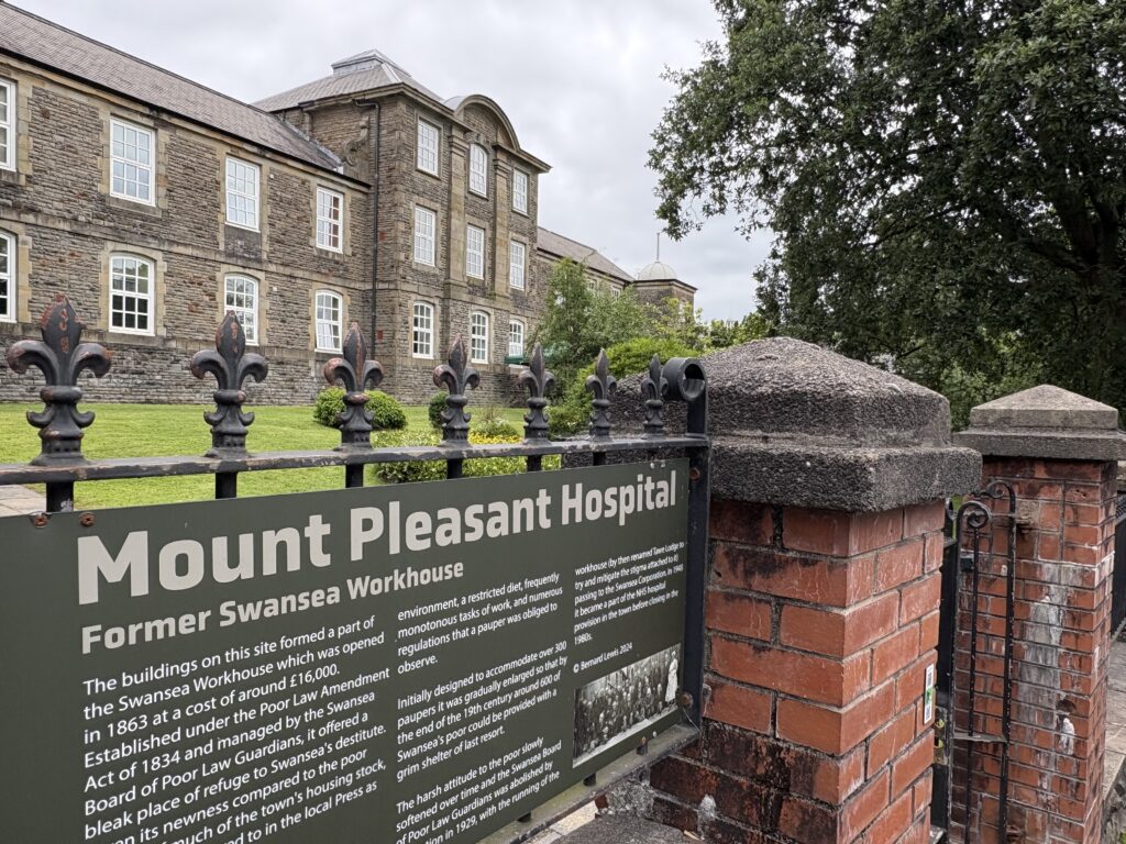 Sign saying Mount Pleasant Hospital with building and lush green space in background