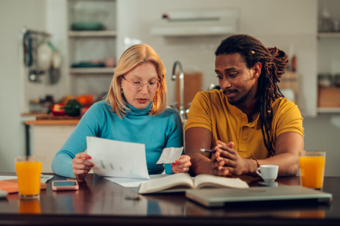 Roedd dyn a menyw yn edrych ar waith papur yn eistedd wrth fwrdd