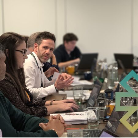Members of Beacon staff and non-executive directors seated around a table interacting and logo element